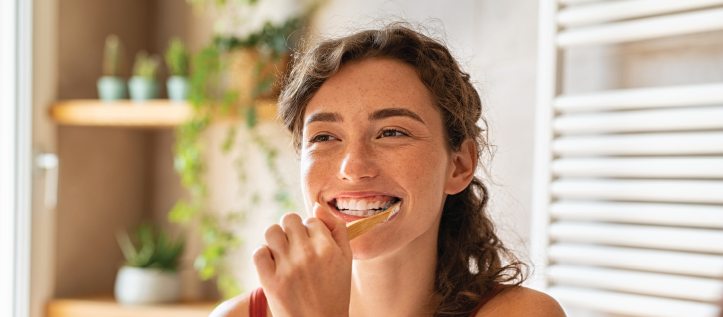 Young woman brushing her teeth and looking in the mirror smiling