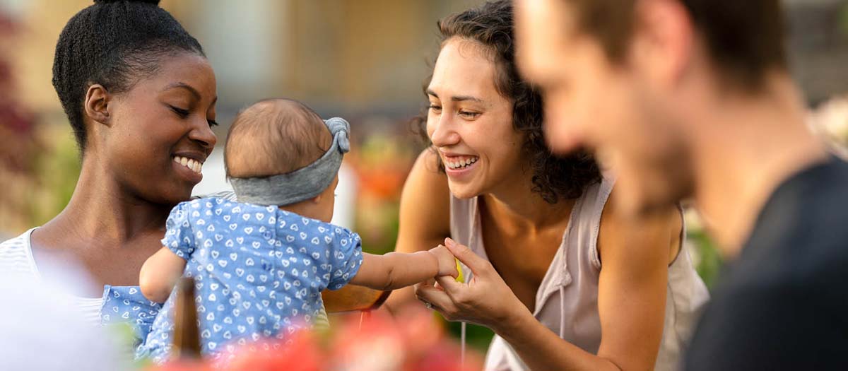 Woman holding a baby as the child reaches towards a friend