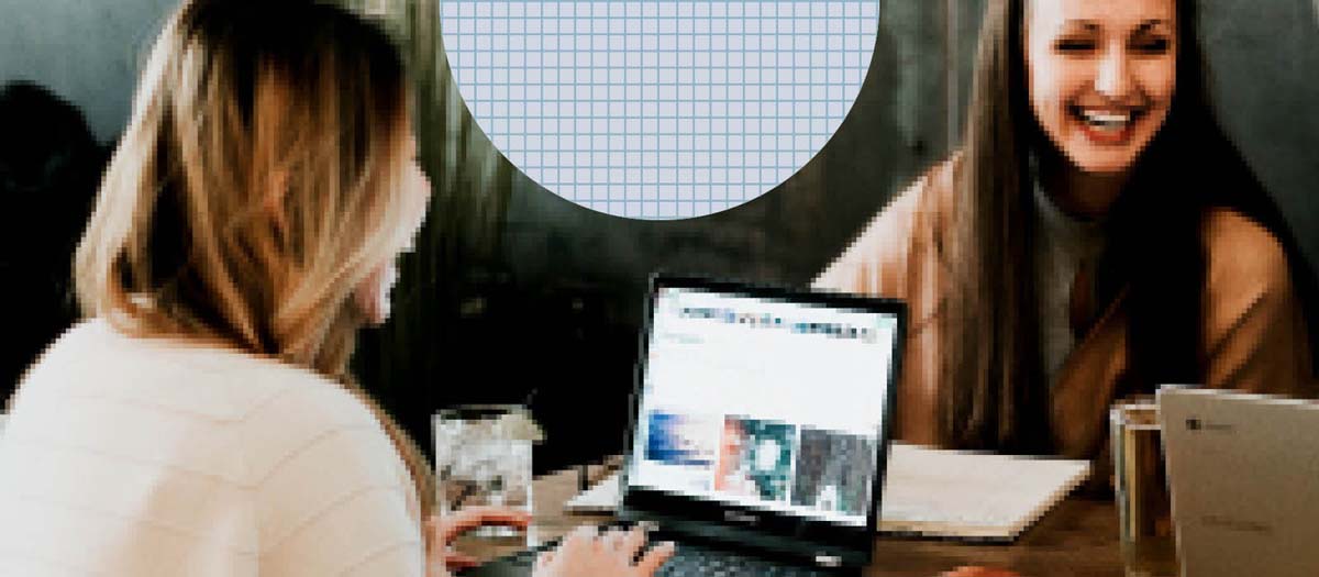 Two girls smiling while doing research on a laptop