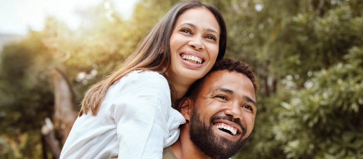 A young couple piggy backing and smiling outdoors.