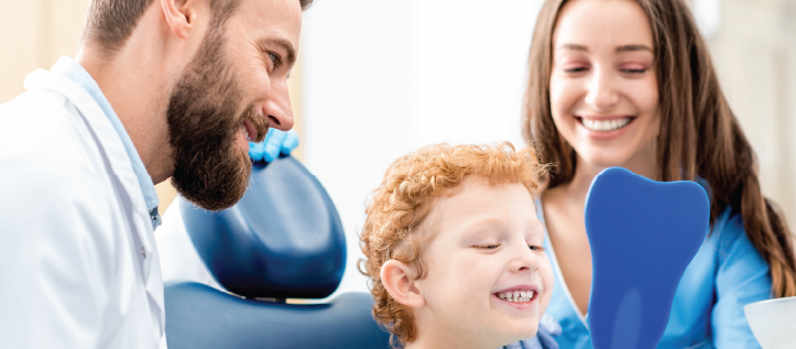 A dentist and a dental hygienist holding a mirror for their young patient as he looks at his teeth