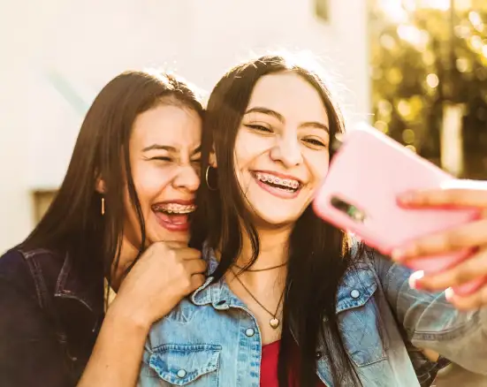 Two teenage girls smiling wearing braces covered by an orthodontic insurance plan