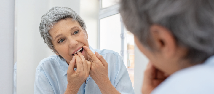 An older woman flossing her teeth looking in the mirror