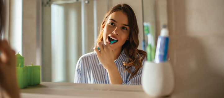 a young woman brushing her teeth looking in the mirror